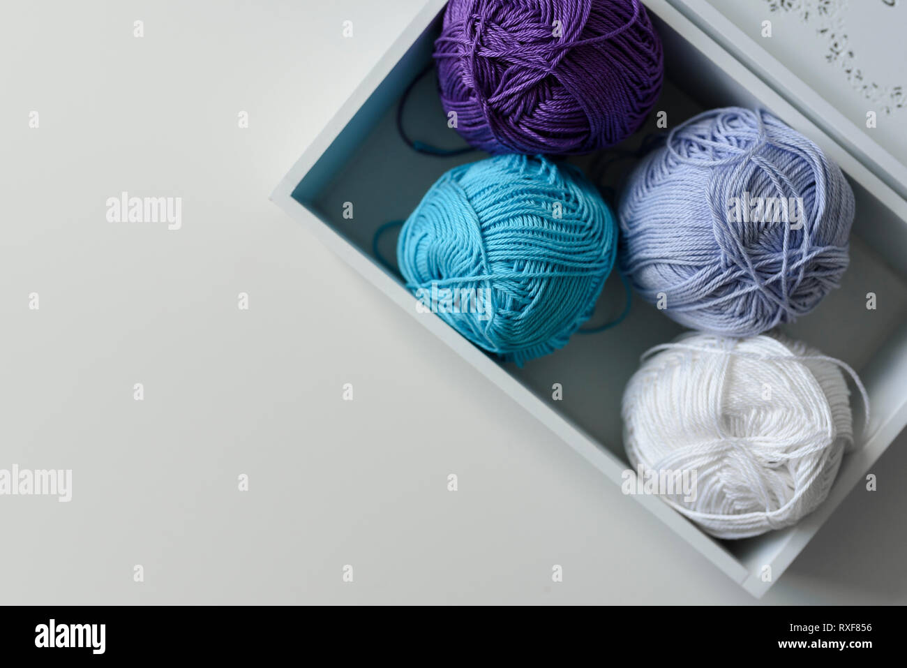 Vue de dessus sur violet, bleu et blanc fil à tricoter laines minérales dans un coffret en bois avec une copie de l'espace sur fond blanc. Banque D'Images