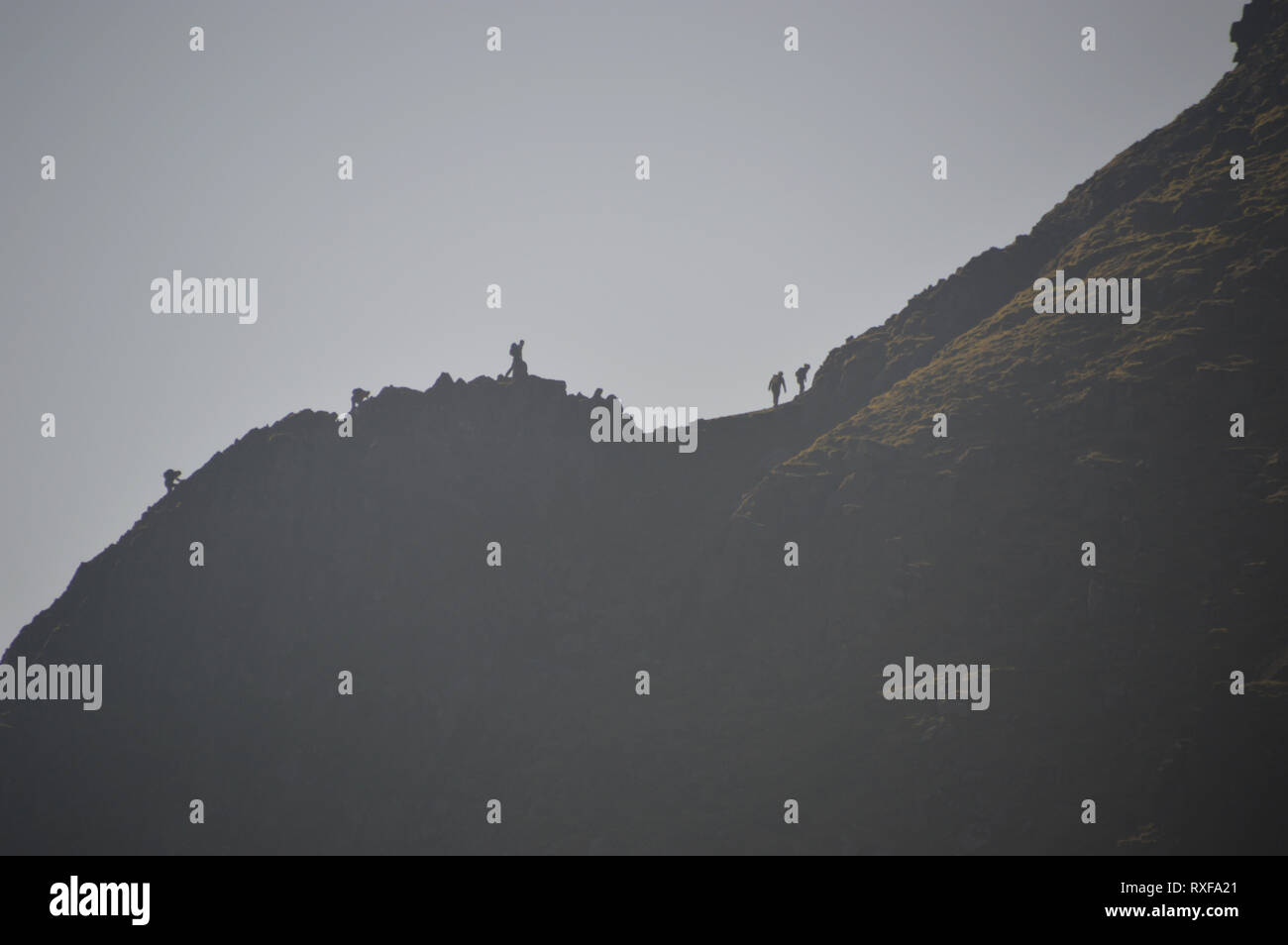 Silhouettes de promeneurs marchant sur l'escalade sur le bord de la route dans l'Helvellyn Wainwright Parc National de Lake District, Cumbria, England, UK. Banque D'Images