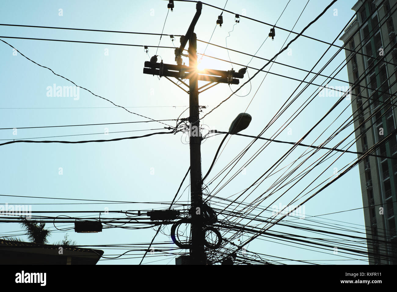 Low angle view of post concrètes pour lampe de rue et de fils électriques au crépuscule. Réseau de câbles en silhouette accrochée à un poteau dans la ville de Panama. Co Banque D'Images