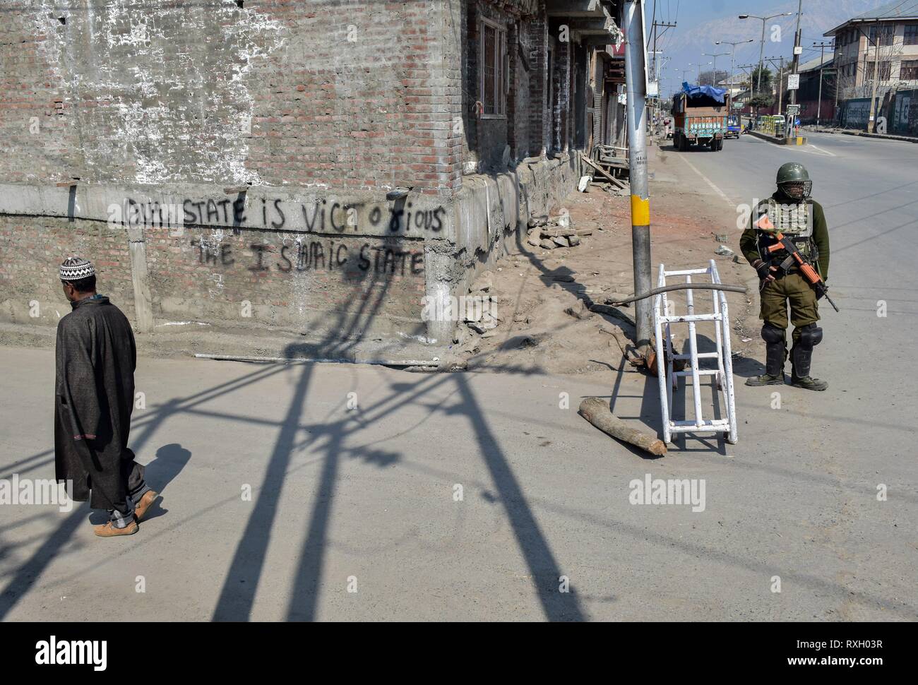 Srinagar, Inde. 10 mars 2019. - Un homme vu marcher le long d'une rue comme un soldat monte la garde au cours de paramilitaires à l'arrêt dans la vieille ville de Srinagar au Cachemire.un arrêt complet est observée dans la vieille ville de Srinagar à protester contre le National Investigation Agency (NIA) convoquer au chef du Cachemire et clerc savant religieux de renommée mondiale Mirwaiz Umar Farooq pour interrogatoire dans sa sonde dans le cas du financement de la terreur. ( Crédit : ZUMA Press, Inc./Alamy Live News Banque D'Images