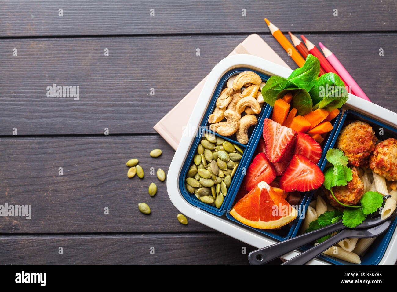 Boîte à lunch pour l'école. Préparation des repas sains avec des boulettes de haricots des conteneurs, pâtes, légumes, petits fruits, graines et noix dans un récipient sur une sombre backgroun Banque D'Images