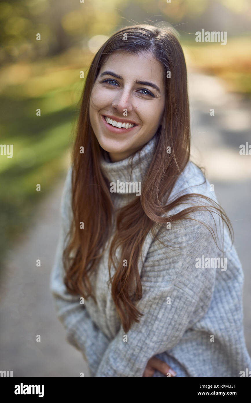 Jolie jeune femme à la mode rétro éclairage en soirée par le soleil debout sur le côté regardant la caméra avec un beau sourire amical dans une autu Banque D'Images