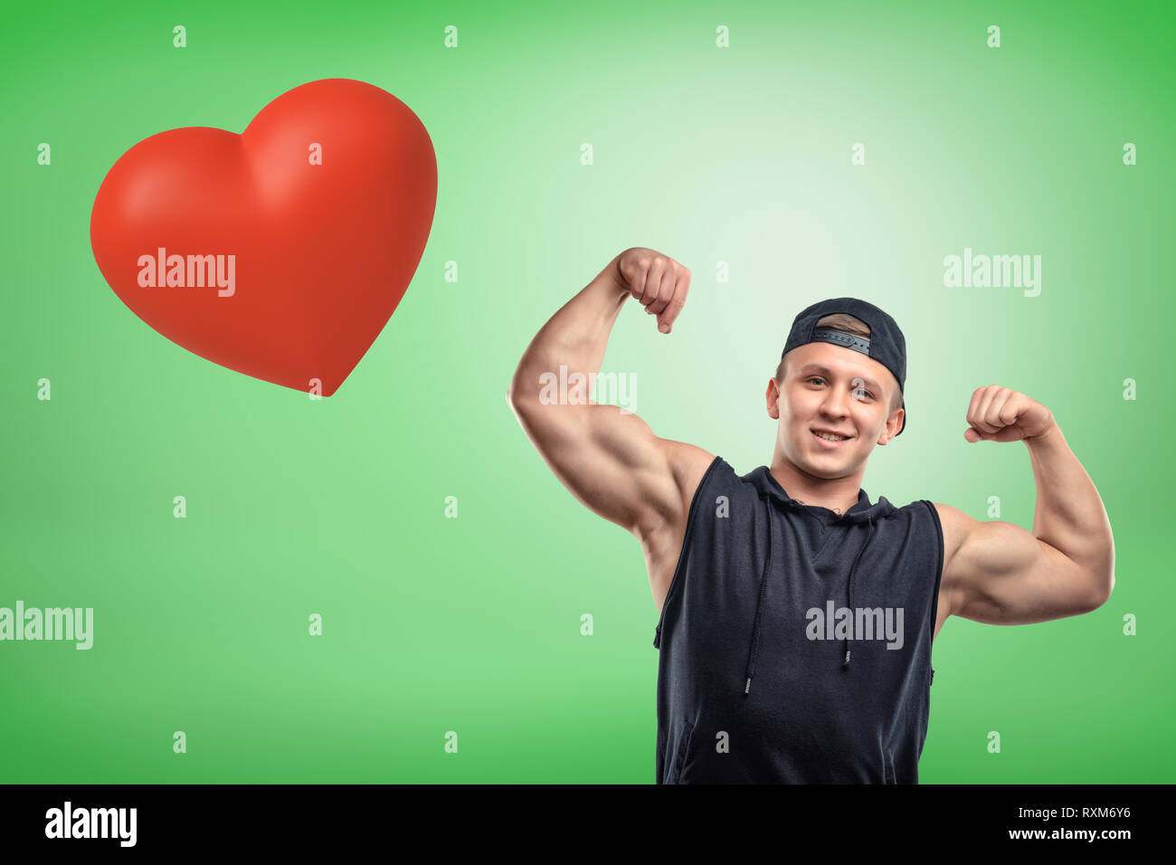 Strong muscular young man showing biceps avec grand cœur rouge sur fond vert Banque D'Images