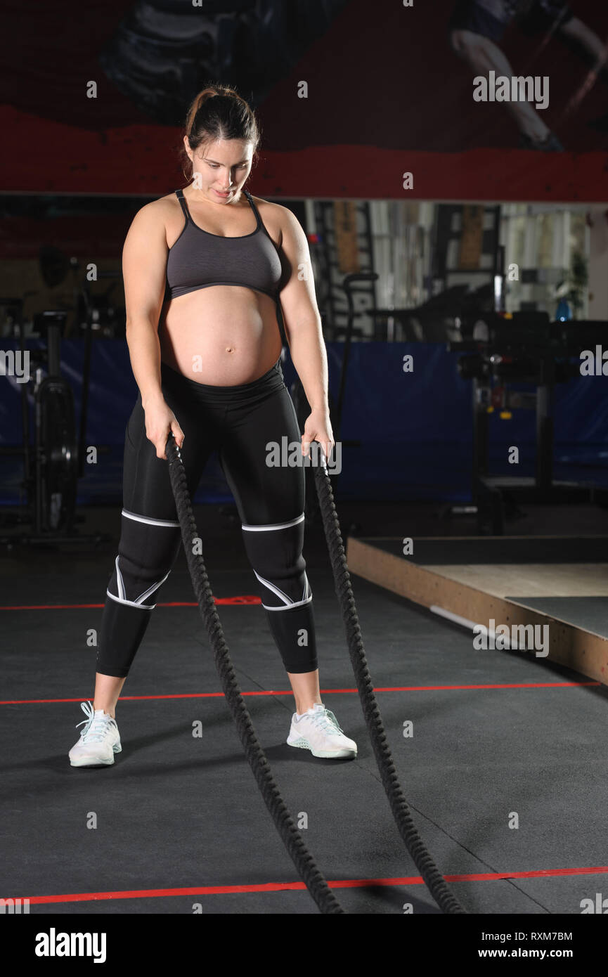 Jeune femme enceinte d'entraînement dur de faire des exercices avec des cordes noires Banque D'Images