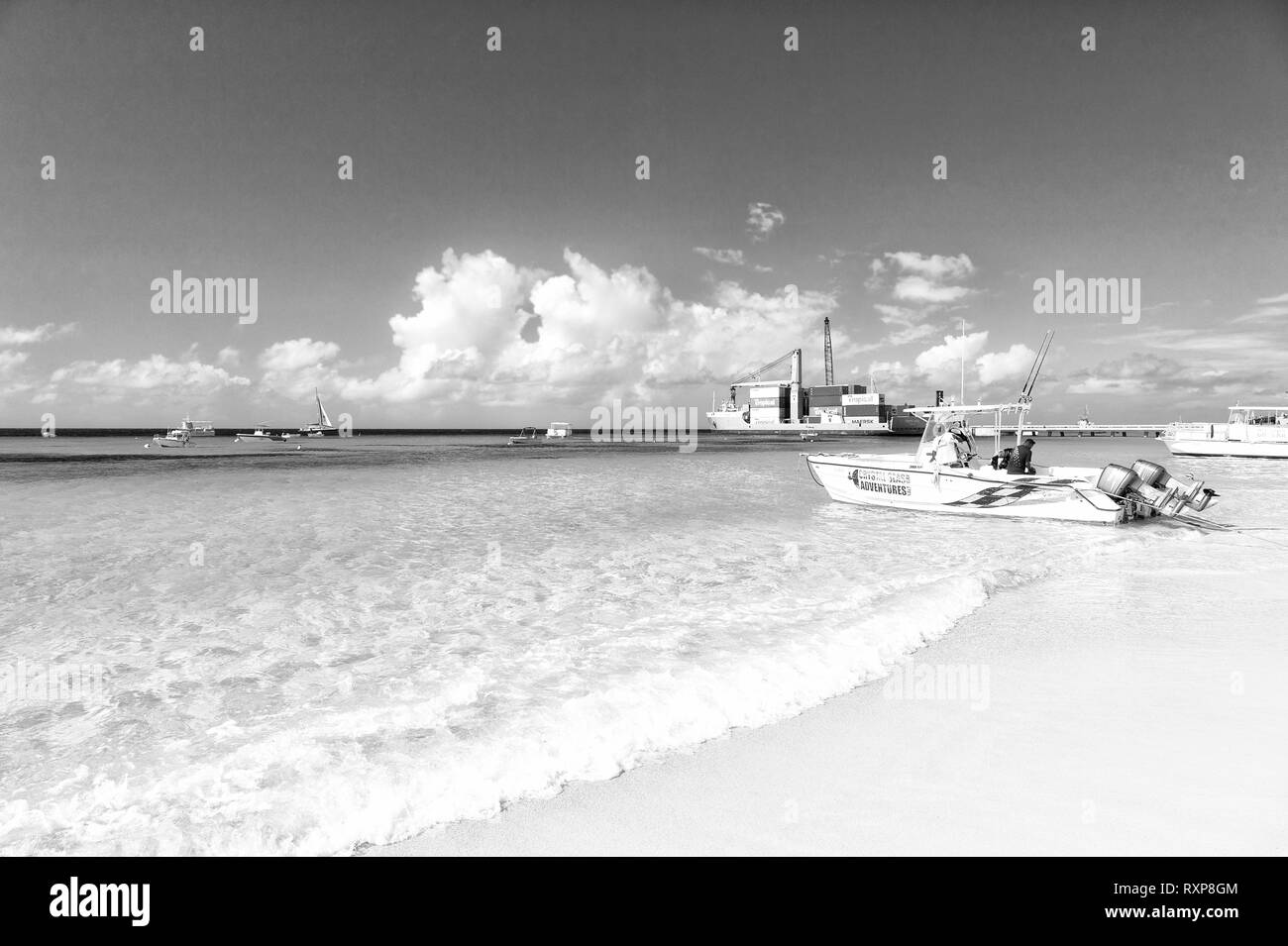 Grand Turk, Îles Turques et Caïques - 29 décembre 2015 : grand cargo couleur rouge avec une grue et de conteneurs sur l'eau de l'océan et bleu ciel nuageux fond, bateau à moteur sur la plage de sable fin piscine ensoleillée Banque D'Images