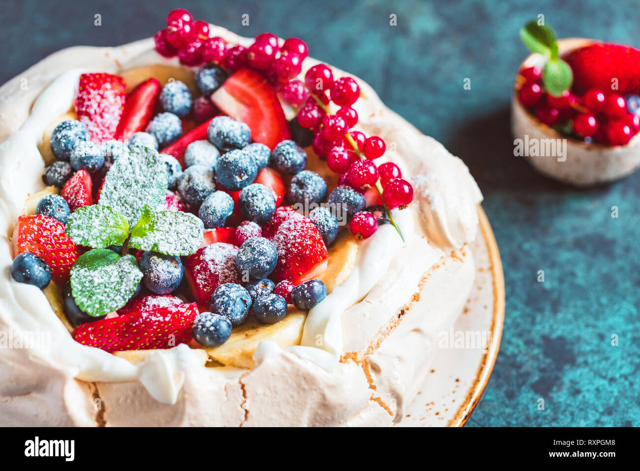 La NOUVELLE ZELANDE Pavlova gâteau avec la crème fouettée et mélange de baies fraîches sur un fond texturé bleu. Banque D'Images