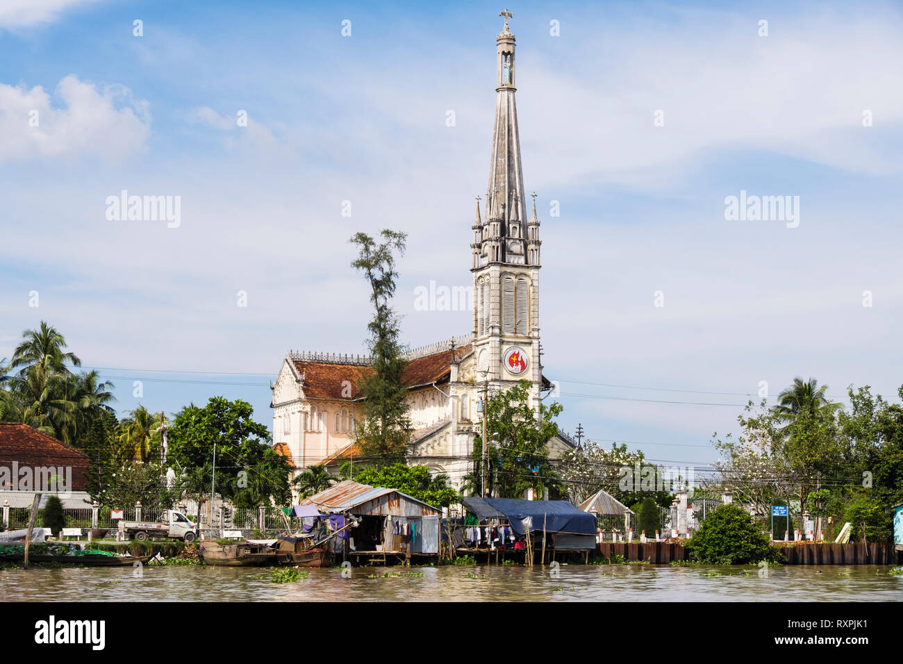20e siècle Cathédrale de l'Église catholique derrière cabane en tôle typique des maisons sur pilotis sur les bords de la rivière Co Chien dans le Delta du Mékong. À Cai Be, Vietnam Banque D'Images