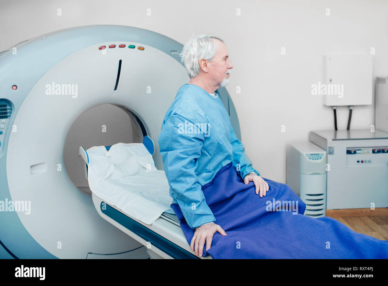 Pensive senior man sitting on table du scanner. en attente de CT scan Banque D'Images