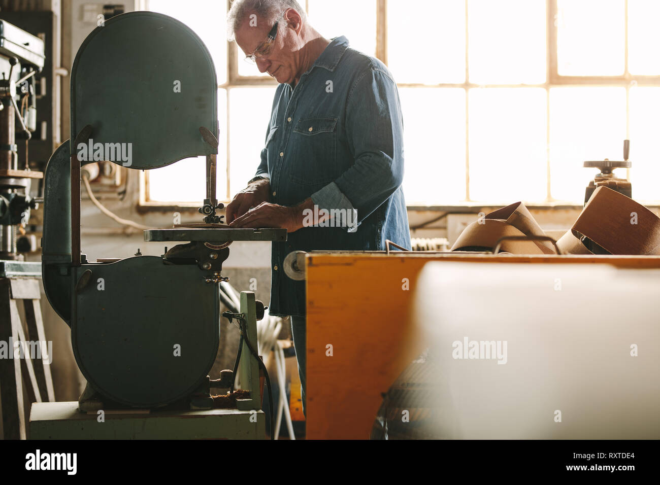 Travailleur senior travaillant sur machine à bande dans son atelier. Menuisier bois de coupe sur la machine à l'atelier de menuiserie. Banque D'Images