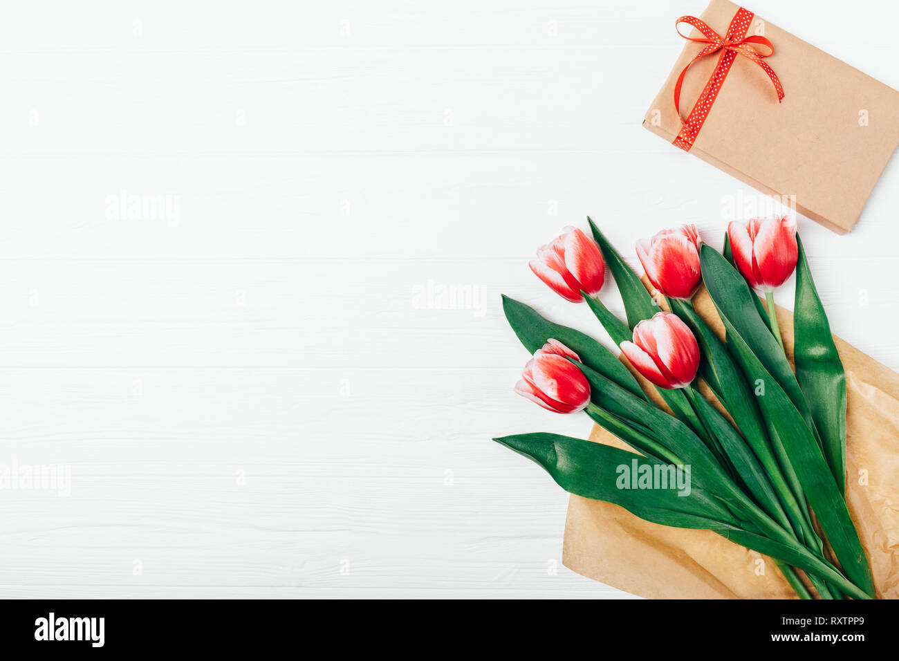 Top View bouquet de belles tulipes rouges dans du papier brun et boîte-cadeau sur fond de bois blanc, copie de l'espace. Banque D'Images