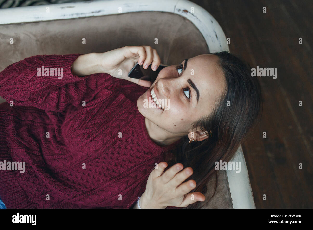 Portrait of young smiling Woman talking on mobile phone on sofa at home. Banque D'Images