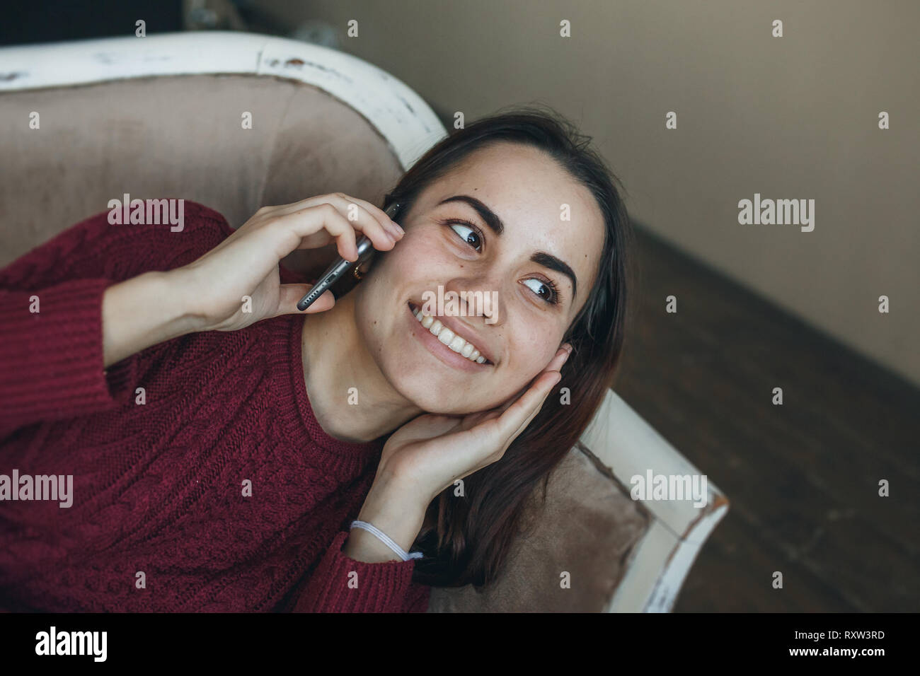 Portrait of young smiling Woman talking on mobile phone on sofa at home. Banque D'Images