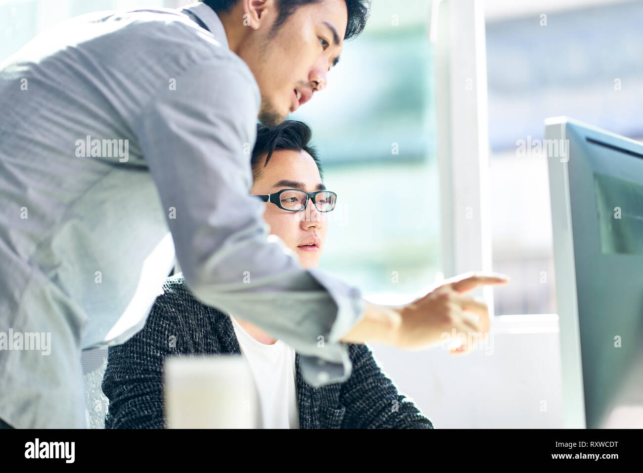 Deux jeunes dirigeants de sociétés asiatiques qui travaillent ensemble à l'aide d'ordinateur de bureau. Banque D'Images