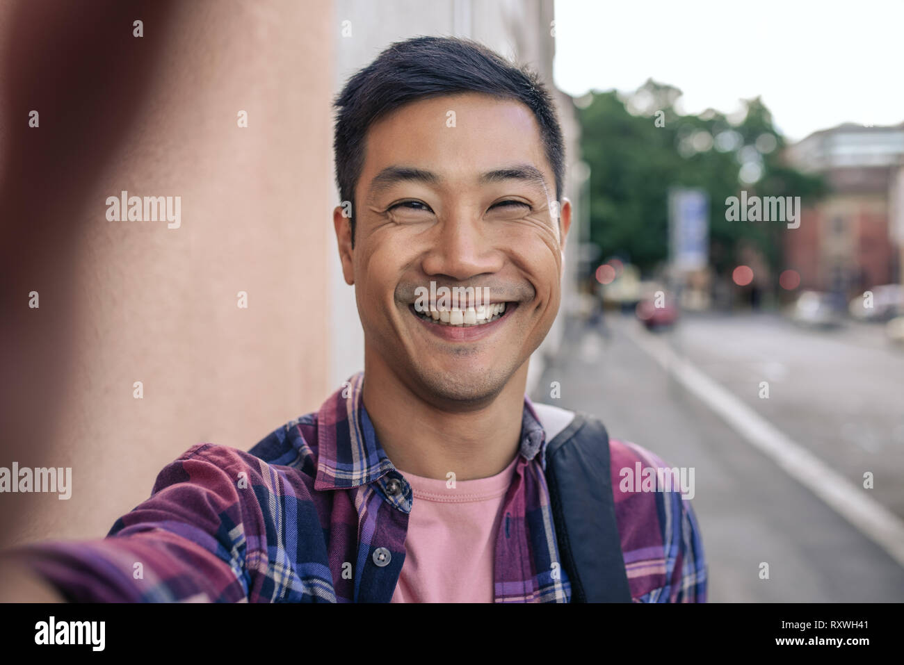 Smiling Young Asian man en tenant vos autoportraits sur une rue de la ville Banque D'Images