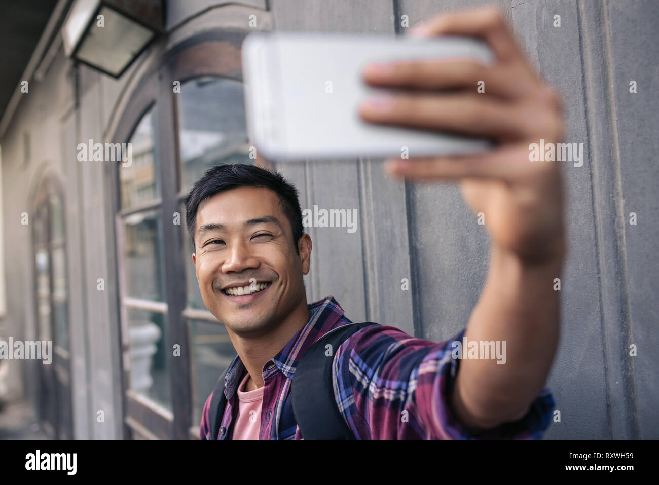 Young Asian man smiling tout en prenant vos autoportraits à l'extérieur Banque D'Images