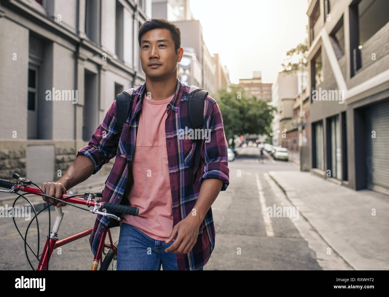Young Asian man walking avec son vélo à travers la ville Banque D'Images