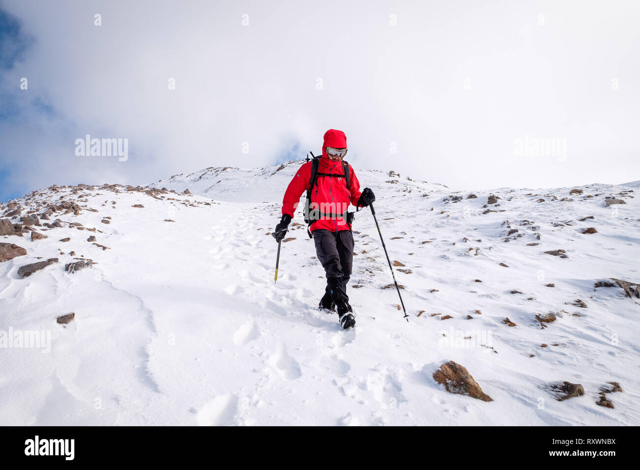 L'homme à la veste rouge, avec piolet randonnée / Escalade en hiver sur la montagne couverte de neige en Ecosse. Modèle libération - Garbh Bheinn, Highlands Loch Leven Banque D'Images