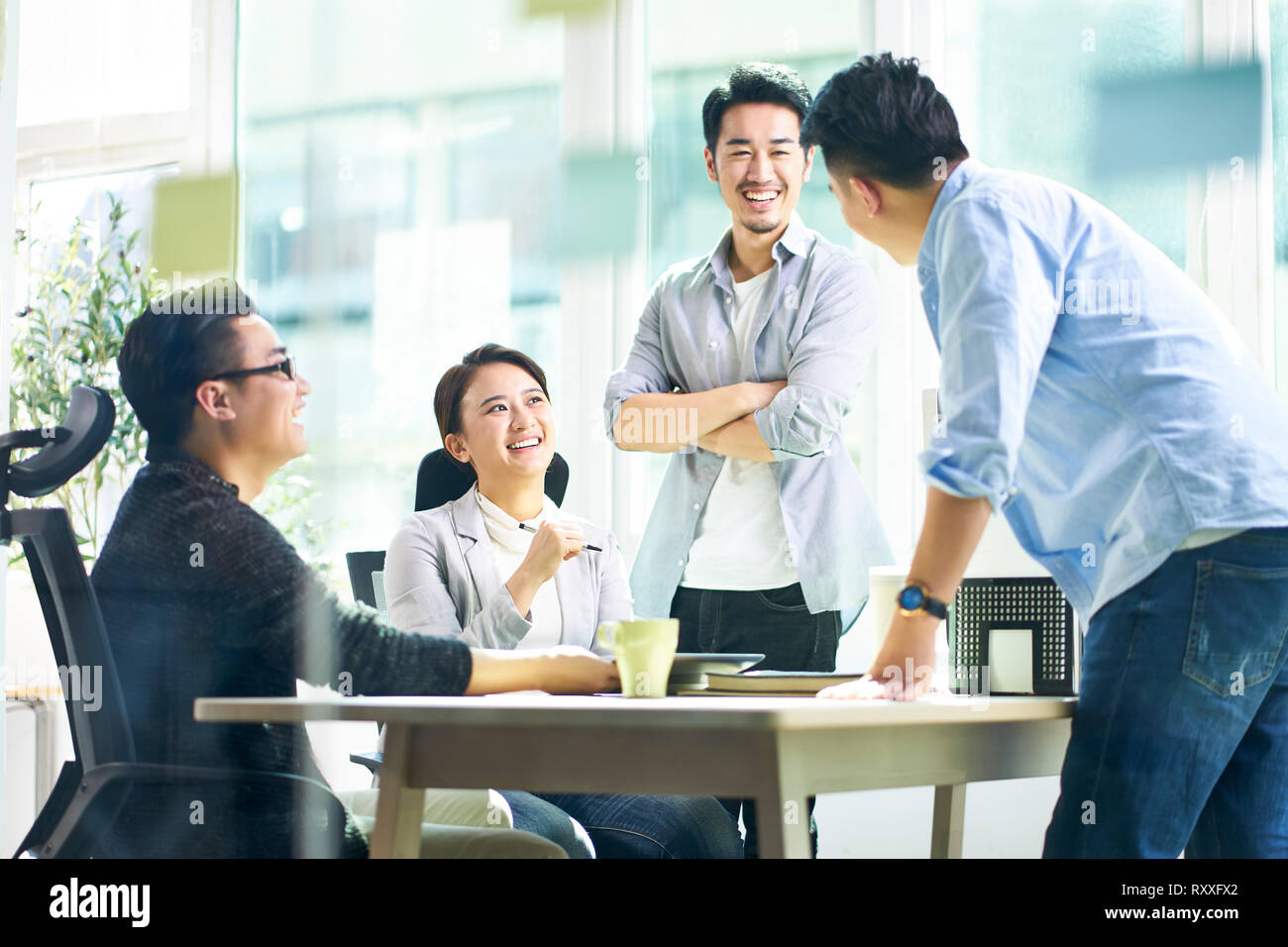 Groupe de quatre jeunes gens heureux d'Asie de l'équipe réunion à discuter des affaires au bureau. Banque D'Images