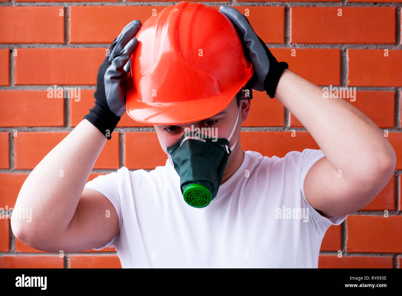 Un homme dans un casque et un masque respiratoire effectue des travaux de  peinture sur un plafond en béton, sur un fond de maçonnerie. Le concept est  monté sur la sécurité au