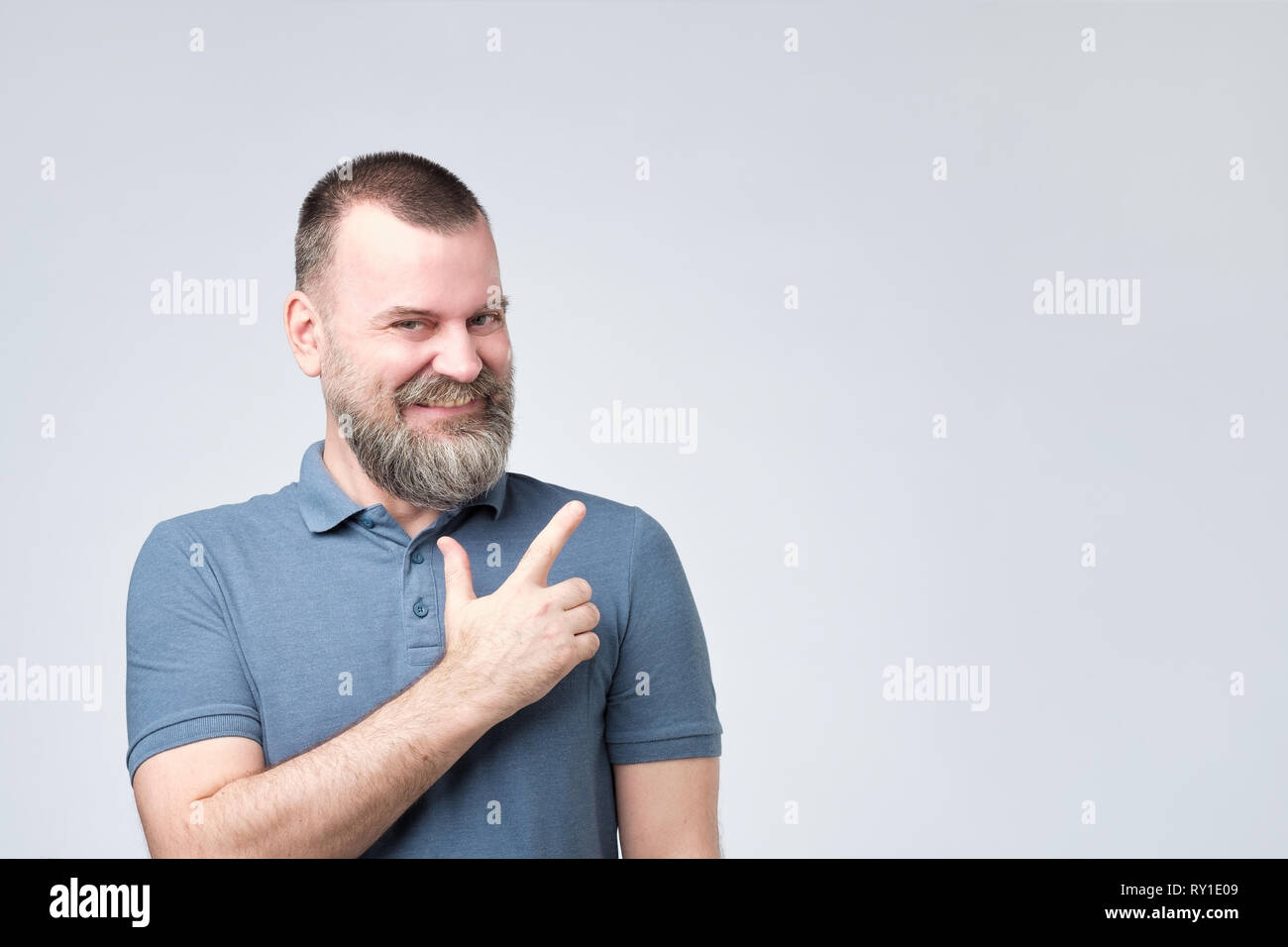 Homme fort MAture avec barbe en chemise bleue pointant un côté avec expression visage surpris Banque D'Images