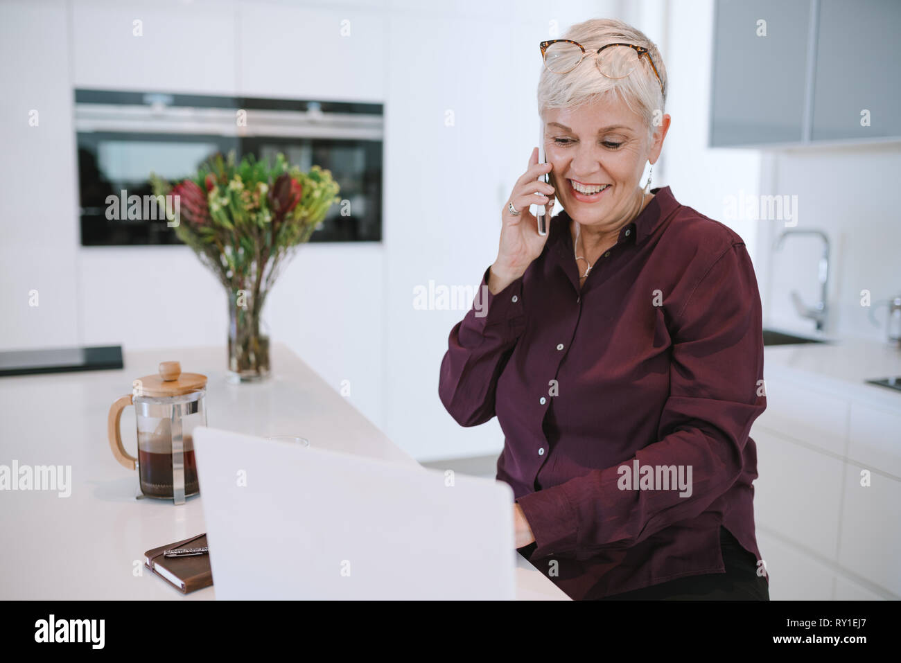 Smiling casual woman using laptop while talking on smartphone. Mature femme travaillant avec un cellulaire et un ordinateur portable à la maison. Femme d'affaires u Banque D'Images