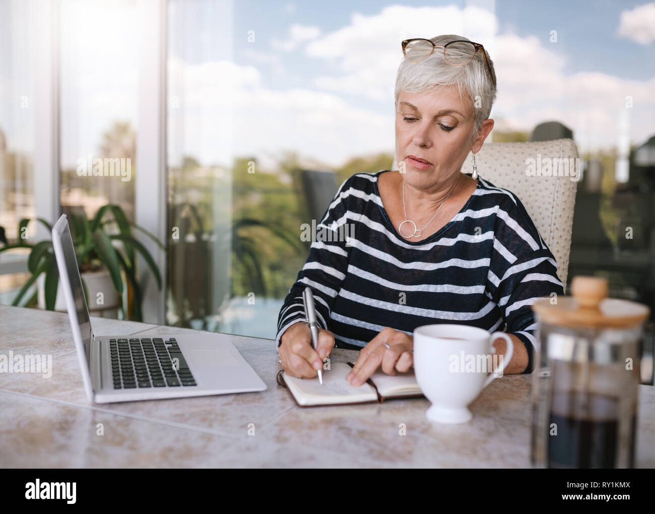 Belle femme mature de prendre des notes tout en travaillant sur son ordinateur portable à la maison. Femme âgée a écrit dans son cahier à l'extérieur sur le balcon Banque D'Images