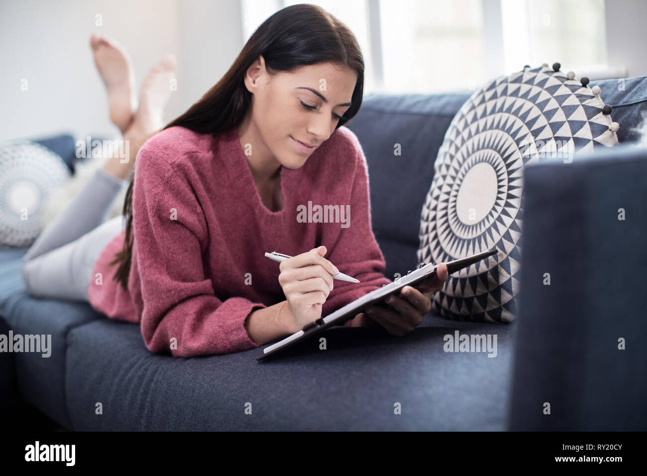 Young Woman Relaxing On Sofa à écrire dans le journal Banque D'Images