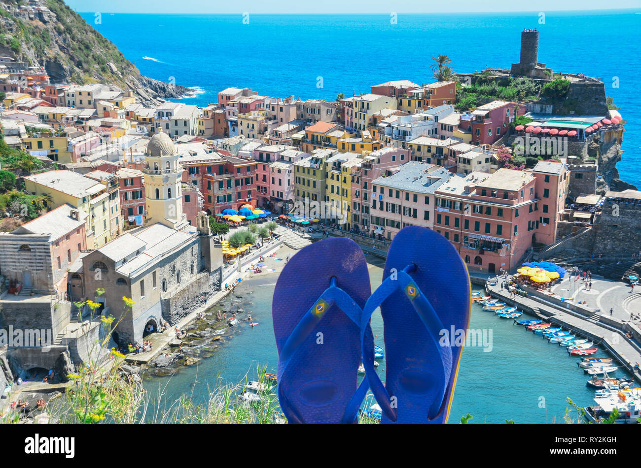 Tongs bleu sur le premier plan avec Vernazza, Cinque Terre - Italie, une destination touristique populaire sur la mer Ligure sur l'arrière-plan - digital composite Banque D'Images