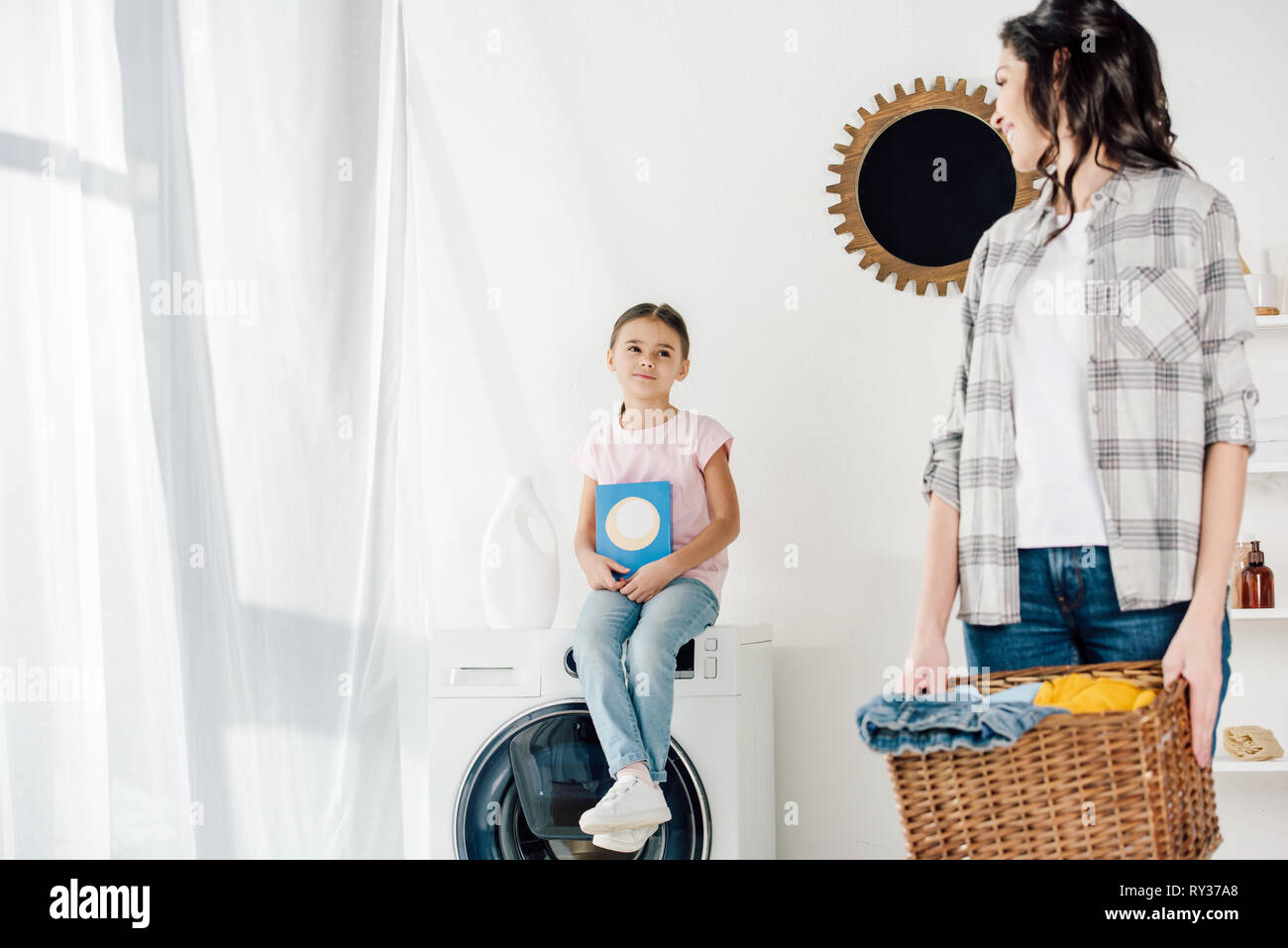 Portrait de fille assis sur la rondelle avec du produit de lavage wile mère  holding basket en salle de lavage Photo Stock - Alamy