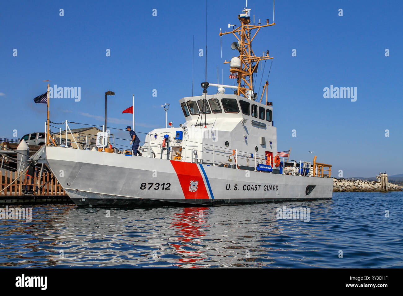 US Coast Guard amarrés au quai des navires avec équipage travaillant sur le pont dans la lumière du soir avec la réflexion sur l'eau Banque D'Images