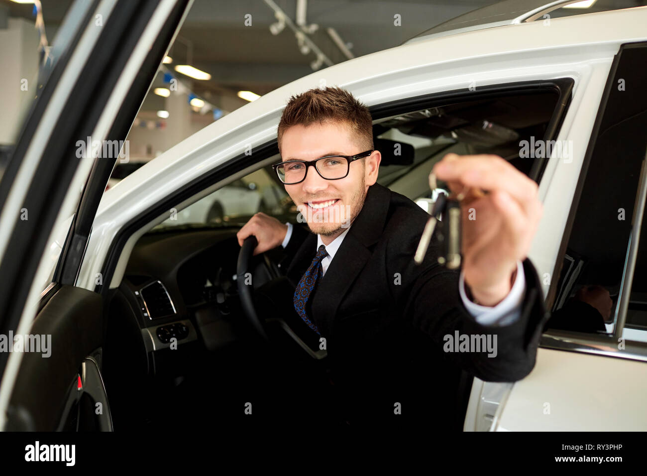 Smiling vendeur détient les clés de voiture en voiture. Banque D'Images