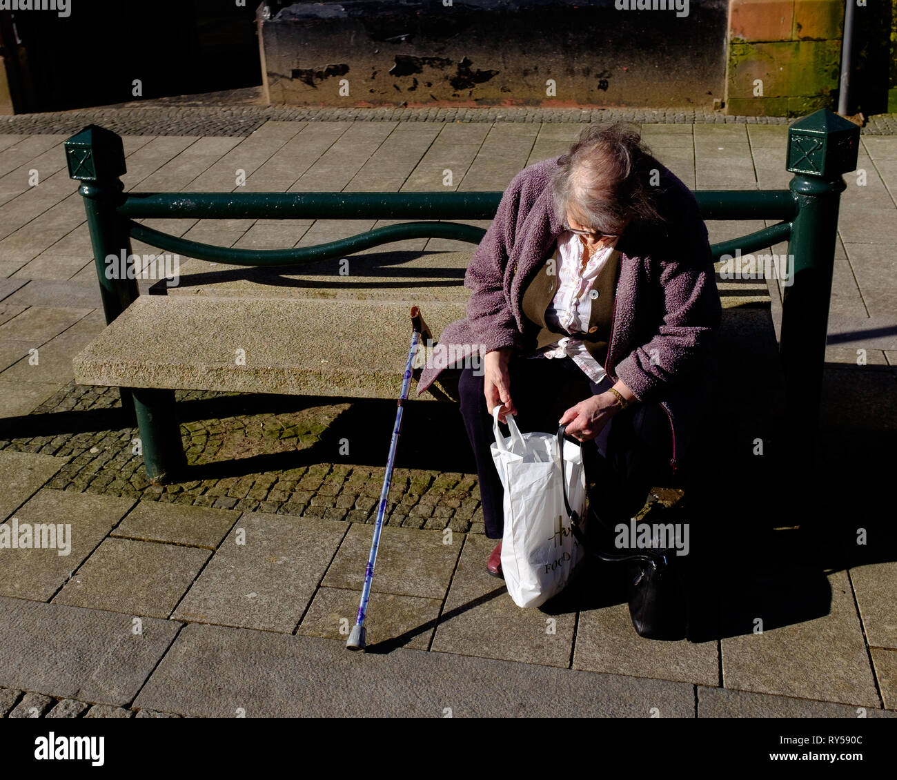 Une femme âgée assise sur banc public à sac shopping en profitant du beau temps dans la région de Fort William lochaber high street Banque D'Images