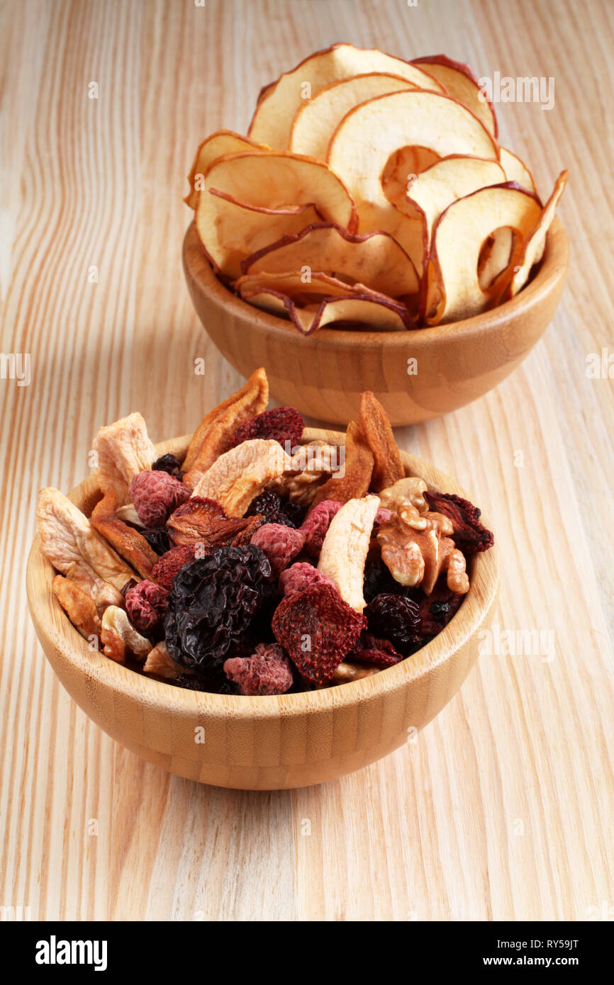 Mélange de fruits secs, morceaux de pomme et poire, prune bleu séchées, fraises, framboises, cerises et noix dans un bol en bambou, et copeaux de pomme dans un Banque D'Images
