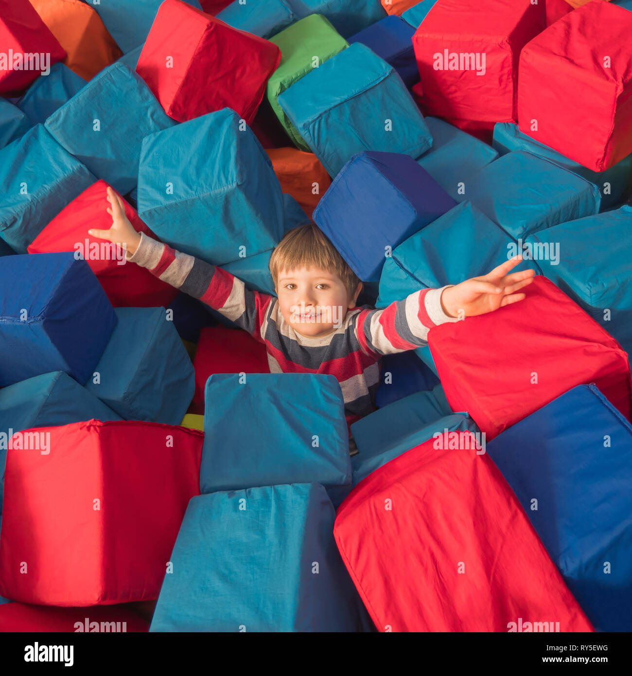Enfance heureuse concept. Garçon jouant avec des blocs dans un centre de divertissement. Kid dans la bonne humeur holding hands up largement l'expression de bonheur. Banque D'Images