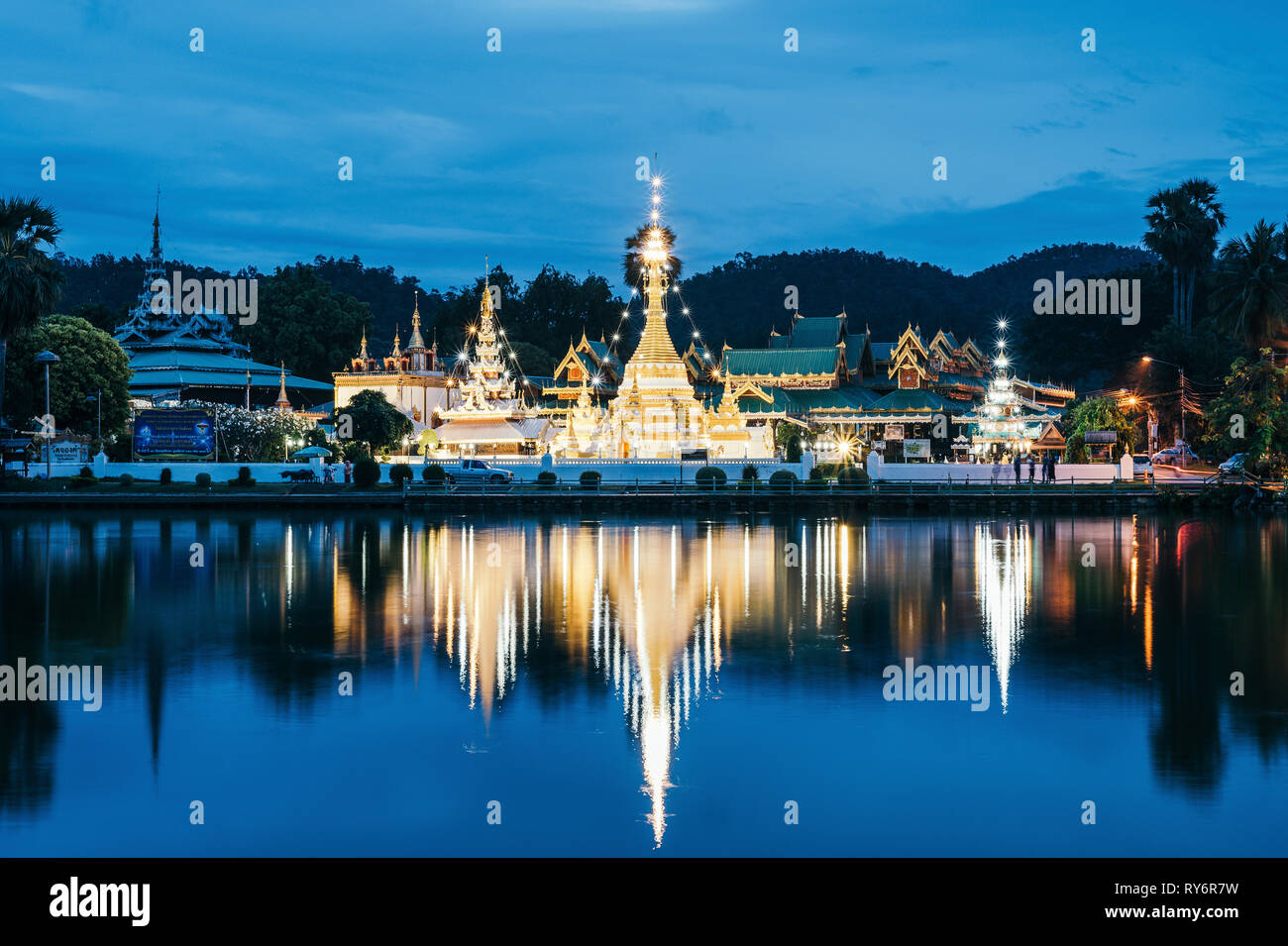 Réflexion sur les temples bouddhistes illuminés lac calme contre ciel nuageux au crépuscule Banque D'Images