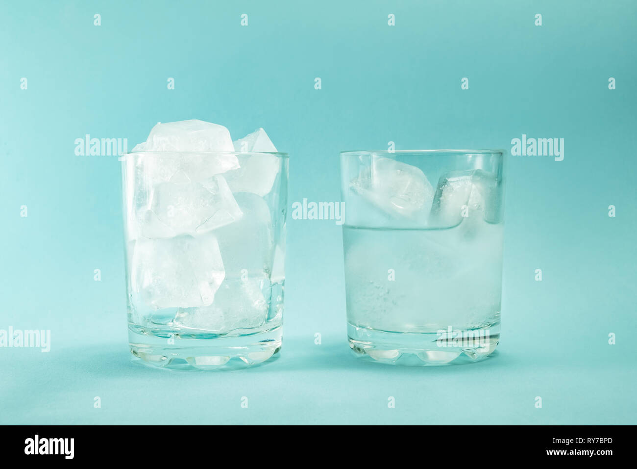 Сoncept du réchauffement global. La fonte de morceaux de glace dans un verre sur un fond bleu. Banque D'Images