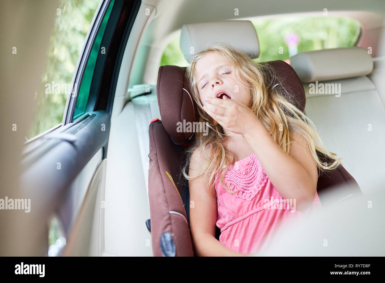 Fille dans la voiture dans le siège enfant sur le siège arrière bâille fatigué sur le voyage Banque D'Images