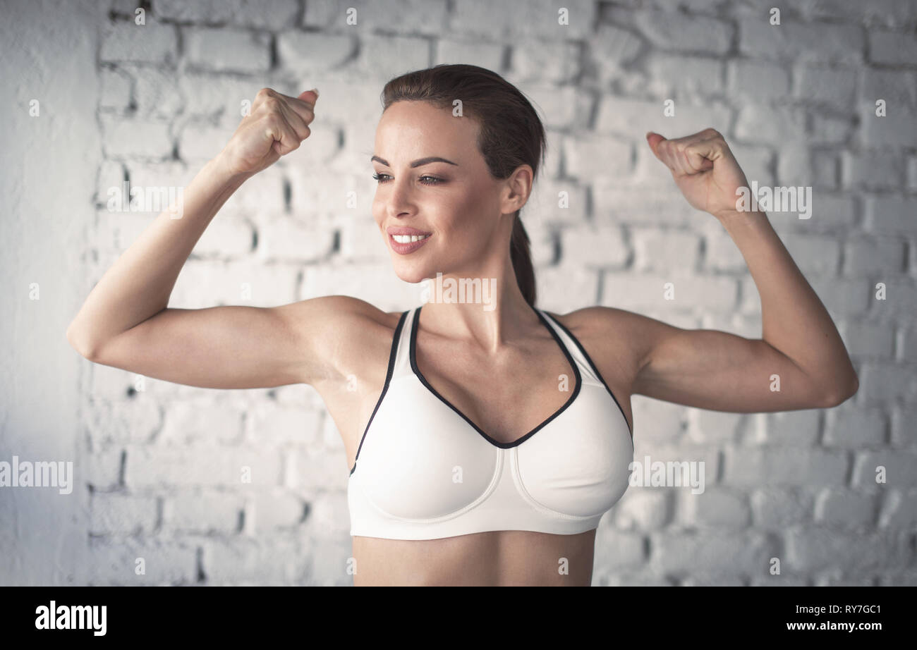 Jeune femme fit forte montrant bicepses portrait dans la salle de sport, à l'écart Banque D'Images
