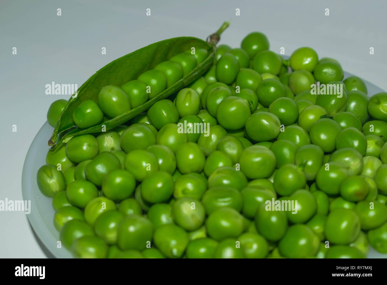 Gousse de pois vert,petits pois dans un bol blanc sur un fond blanc. Banque D'Images