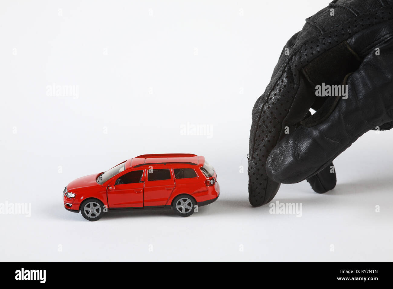 Une main gantée se déplace tranquillement vers une (miniature) voiture pour la voler. Banque D'Images