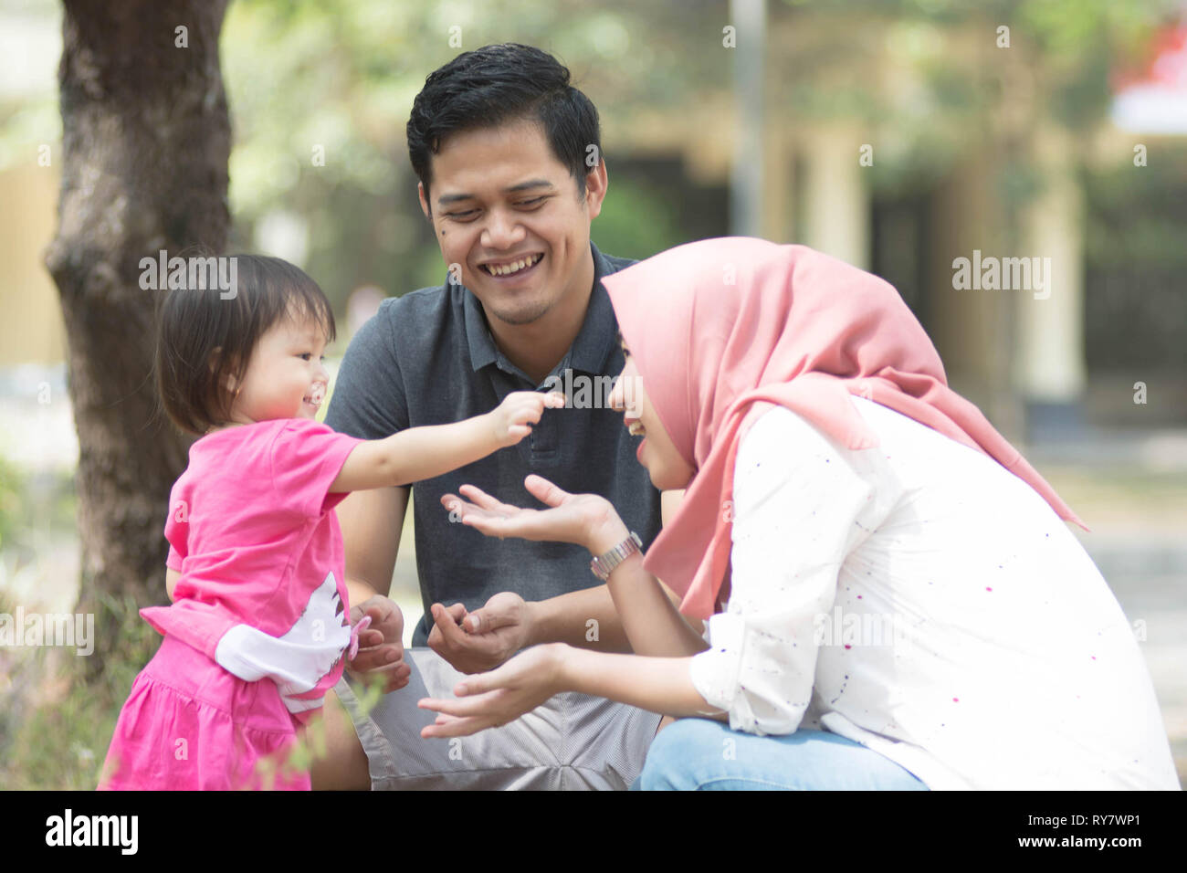 Jeune famille musulmane avec l'un des enfants jouer au parc avec petite fille montrant quelque chose à sa mère à la journée ensoleillée Banque D'Images