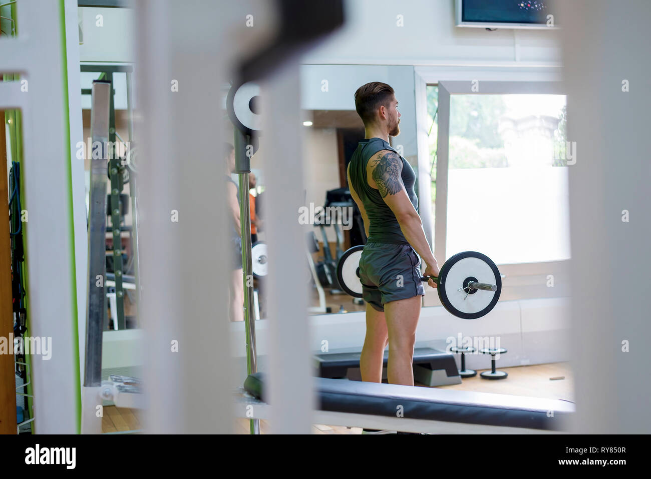 Vue latérale du man lifting barbell tout en se tenant dans une salle de sport Banque D'Images