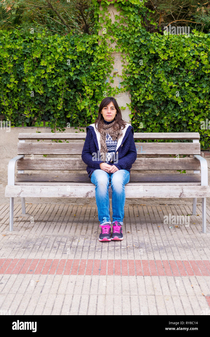 Full Length portrait of young woman sitting on bench in park Banque D'Images