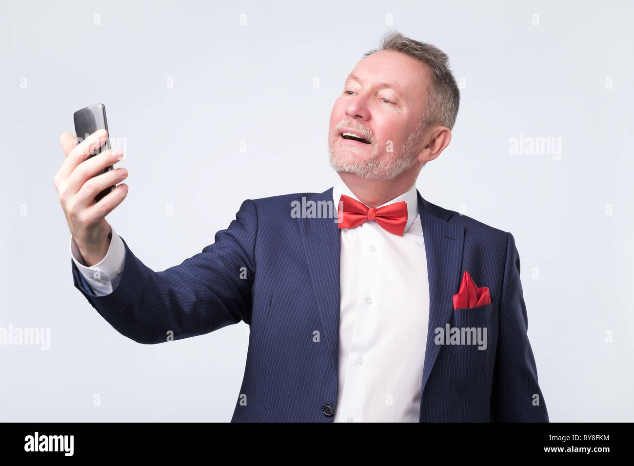 Man au costume bleu à écran de téléphone intelligent, souriant gentiment Banque D'Images