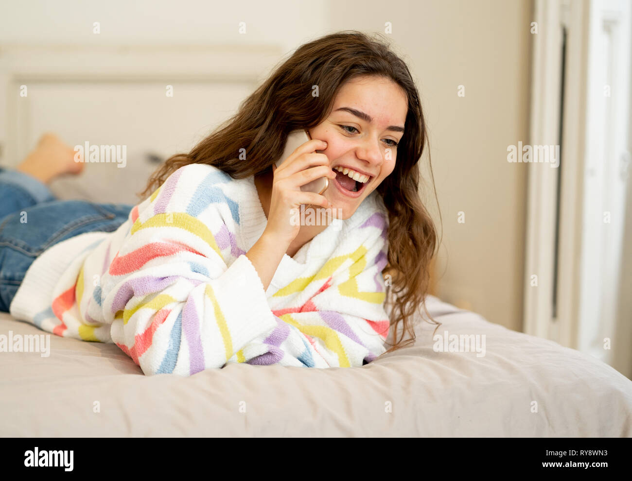 Heureux jeune fille adolescente appelant les smart mobile phone talking and smiling tout en vous relaxant sur le lit chez lui. Dans les gens, la connexion, le mode de vie, co Banque D'Images