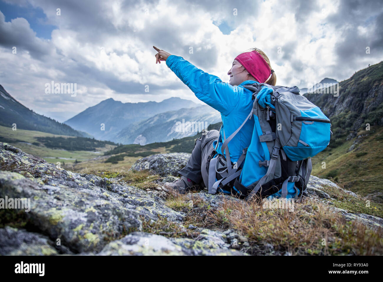 D'alpiniste avec sac à dos est assis sur le sol pierreux et faisant un geste de pointage Banque D'Images