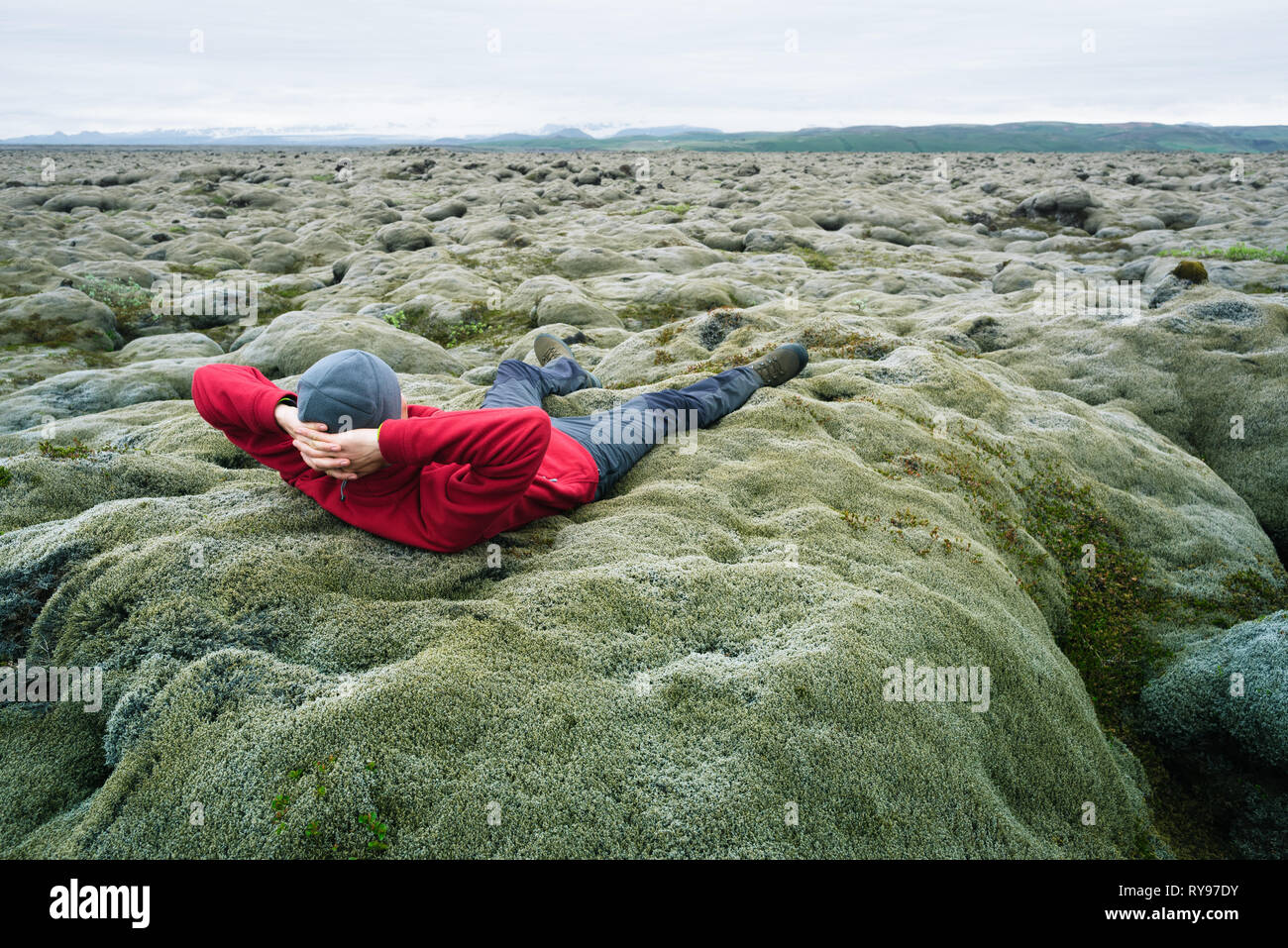 Voyageur dans l'homme veste rouge couché sur la mousse. Champ de lave sur la côte sud de l'Islande, l'Europe. Attraction touristique. Étonnant dans la nature. D'été nuageux Banque D'Images