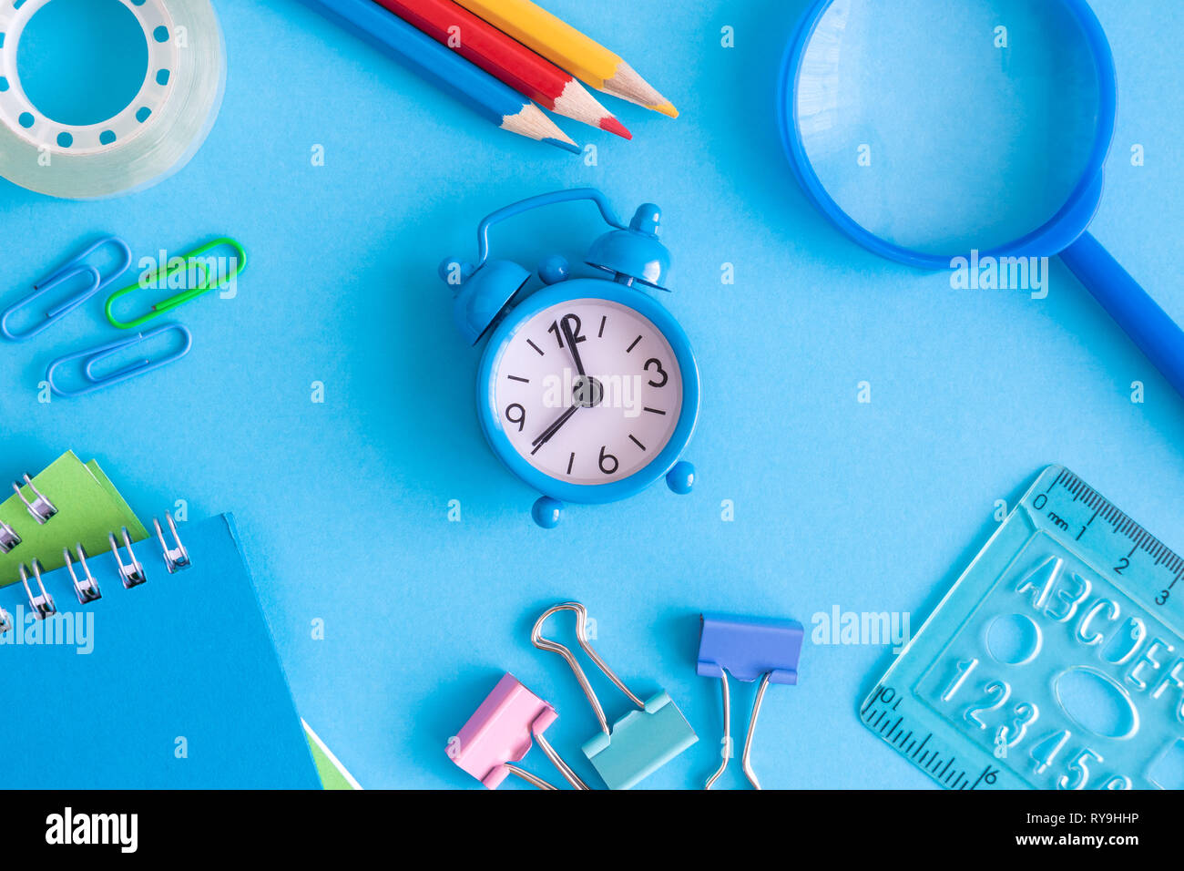 Petit réveil avec les fournitures scolaires sur fond bleu un minimum retour à l'école créative concept. Banque D'Images