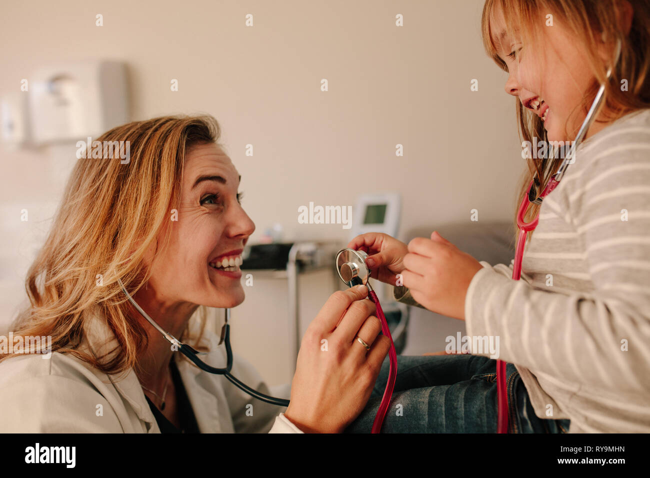 Jeune fille jouant avec sa pédiatre patient. Friendly médecin et de la jeune fille sur rendez-vous chez le médecin, les deux jouant avec stéthoscope. Banque D'Images