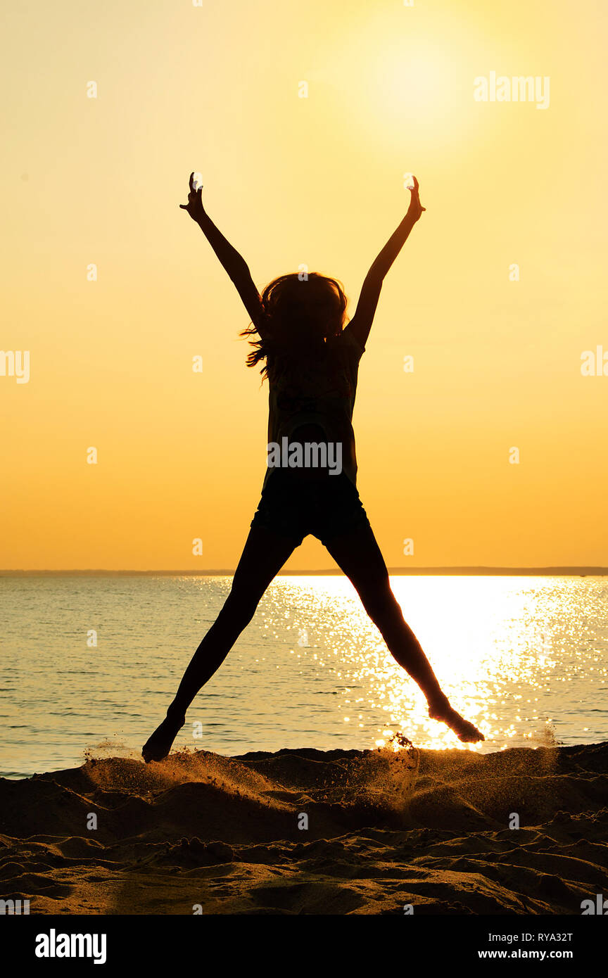 Silhouette d'une fille de saut. L'été sur la plage au coucher du soleil. Banque D'Images